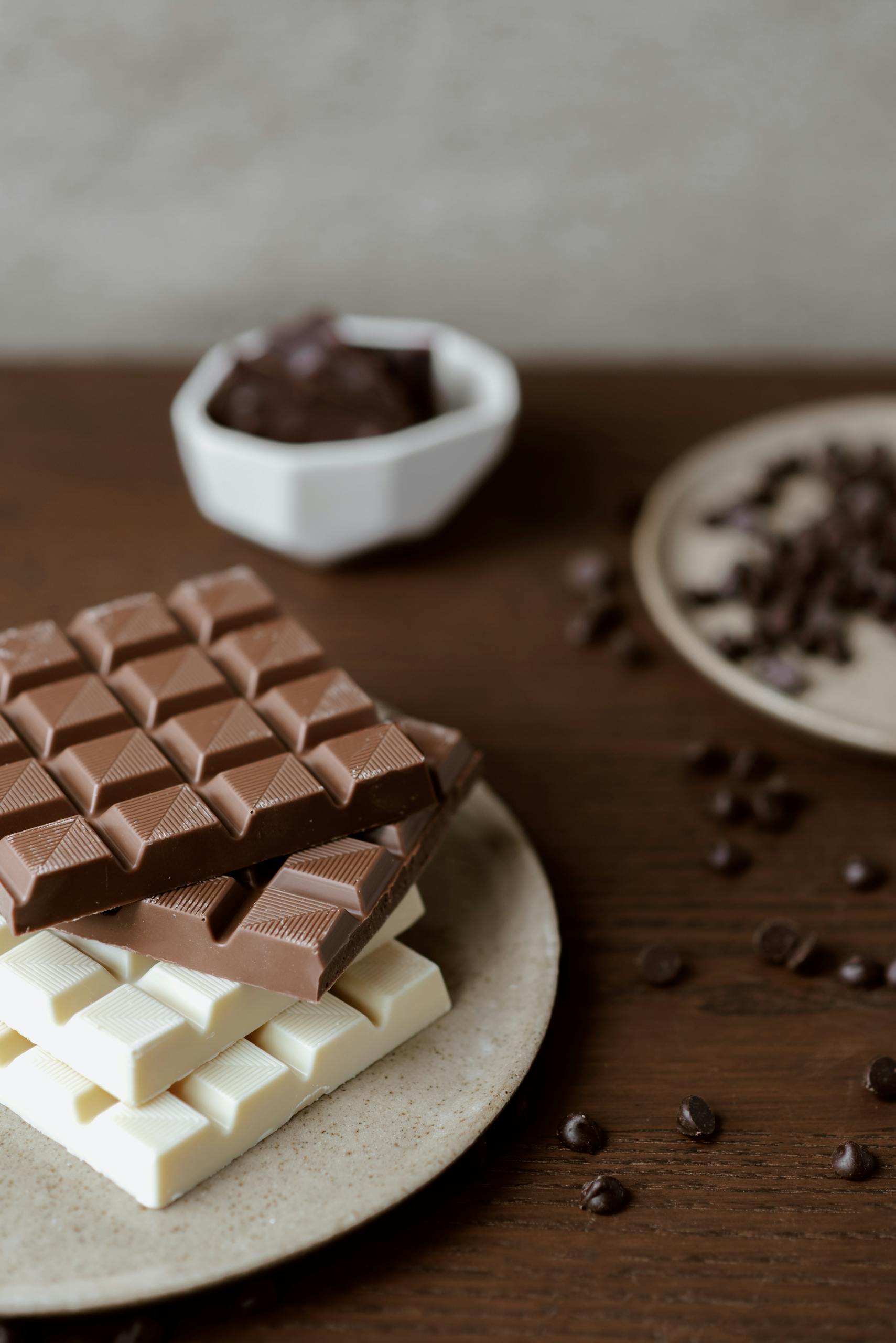 High angle of delicious bars of chocolate on plate on wooden table with scattered chocolate chips
